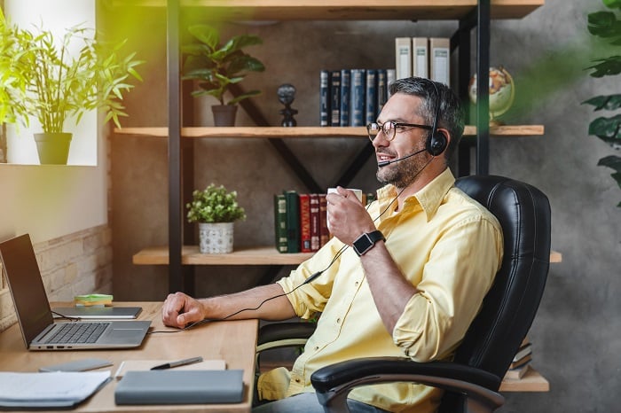 Man working from home at a desk with a cup of coffee in one hand